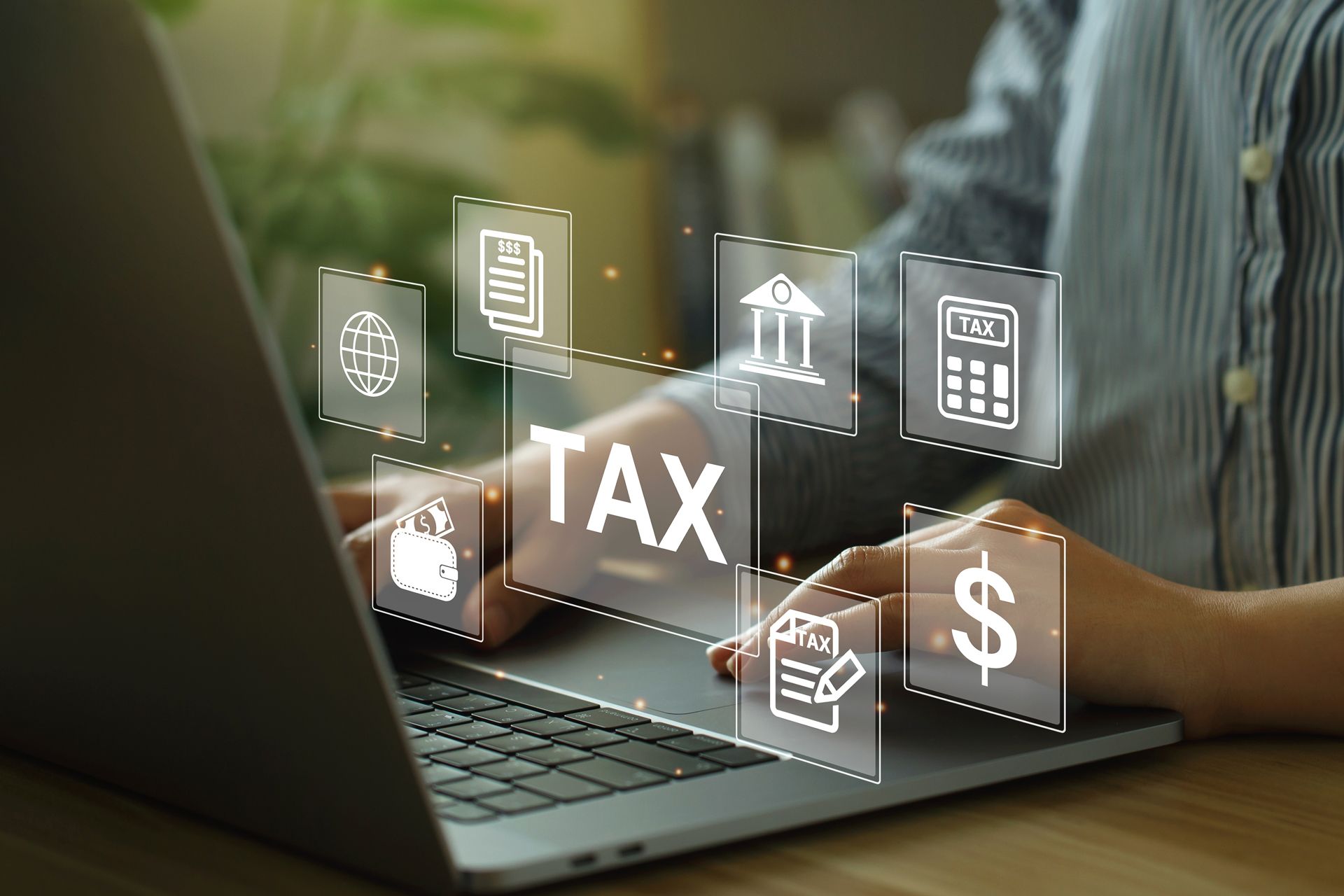 A person is typing on a laptop computer with tax icons coming out of the screen