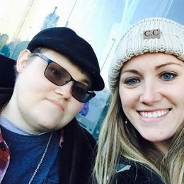 Two people taking a selfie. One wears a black cap and sunglasses, the other a cream beanie.