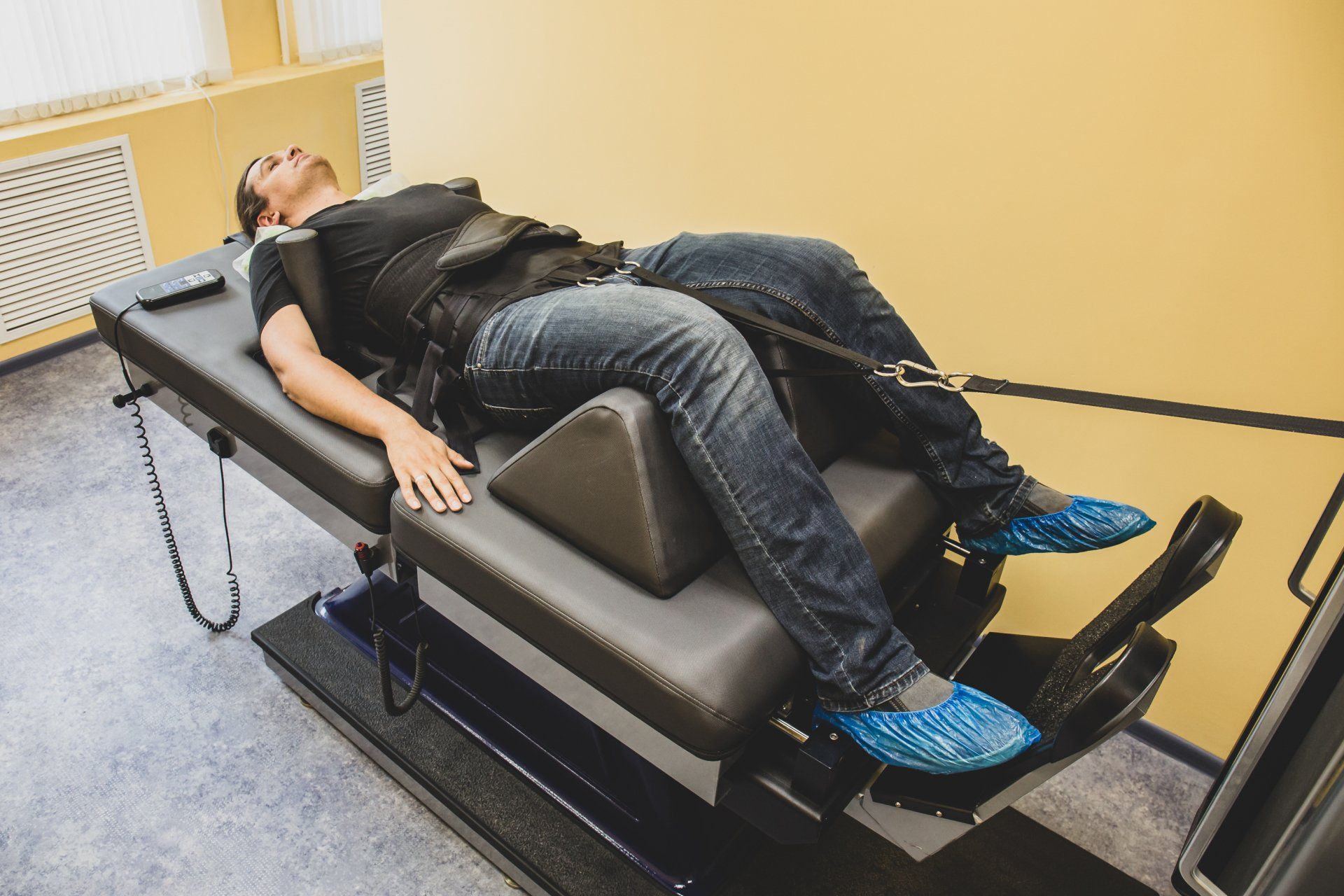 Person lying on a specialized therapy table with legs secured; indoors.