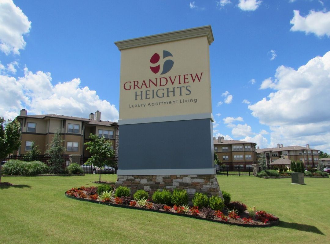 A monument sign for Grandview Heights apartments on a grassy lawn with buildings in the background under a cloudy sky.