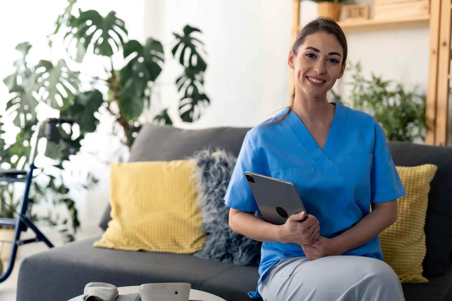 A nurse is sitting on a couch holding a tablet.