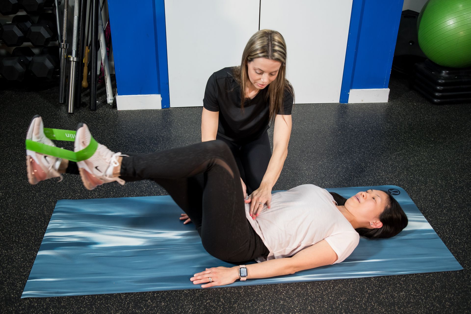 physiotherapist helping woman exercise with bands on her feet on her back