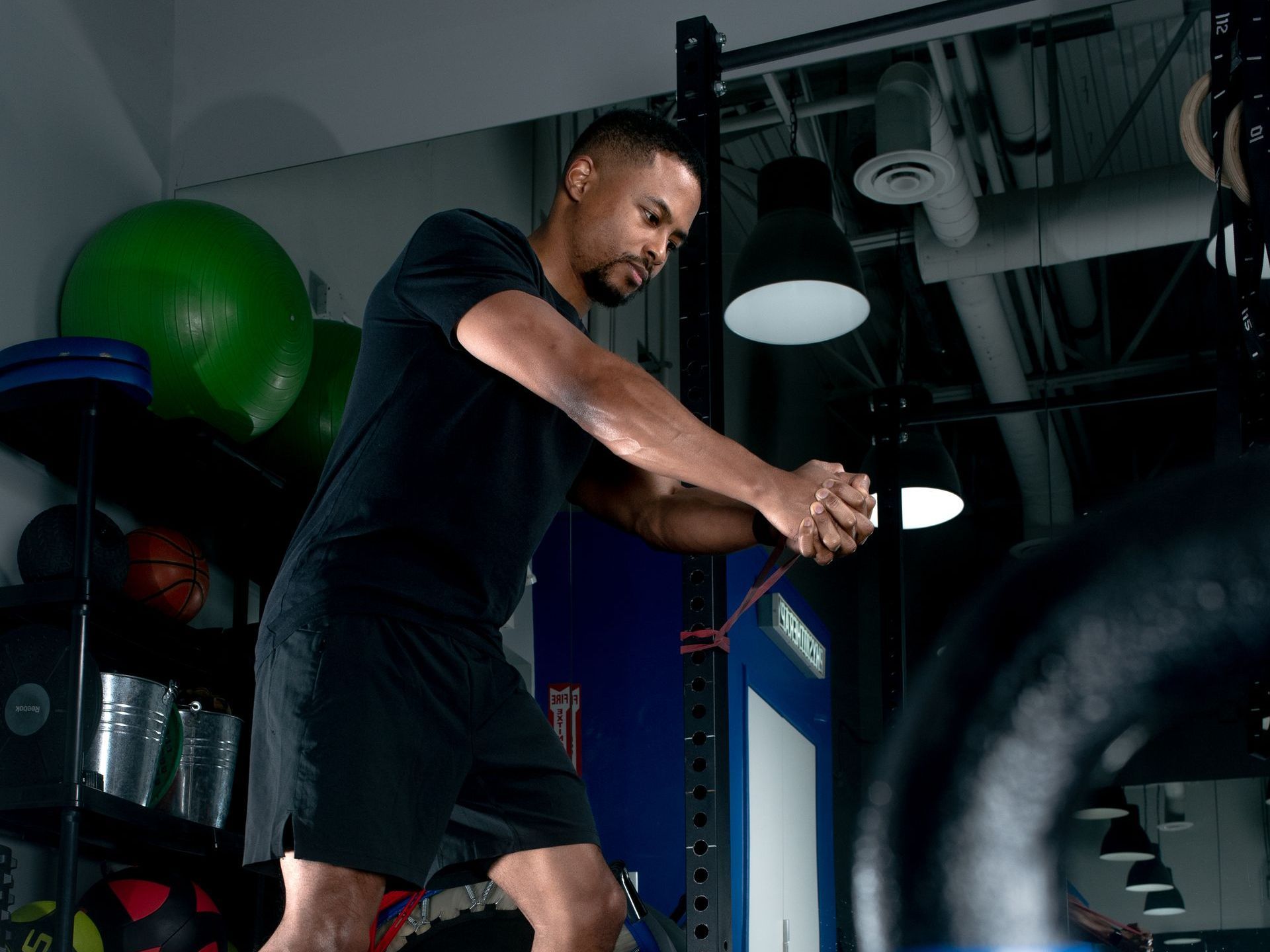 A person performs a resistance band row exercise in a gym with various fitness equipment in the background.