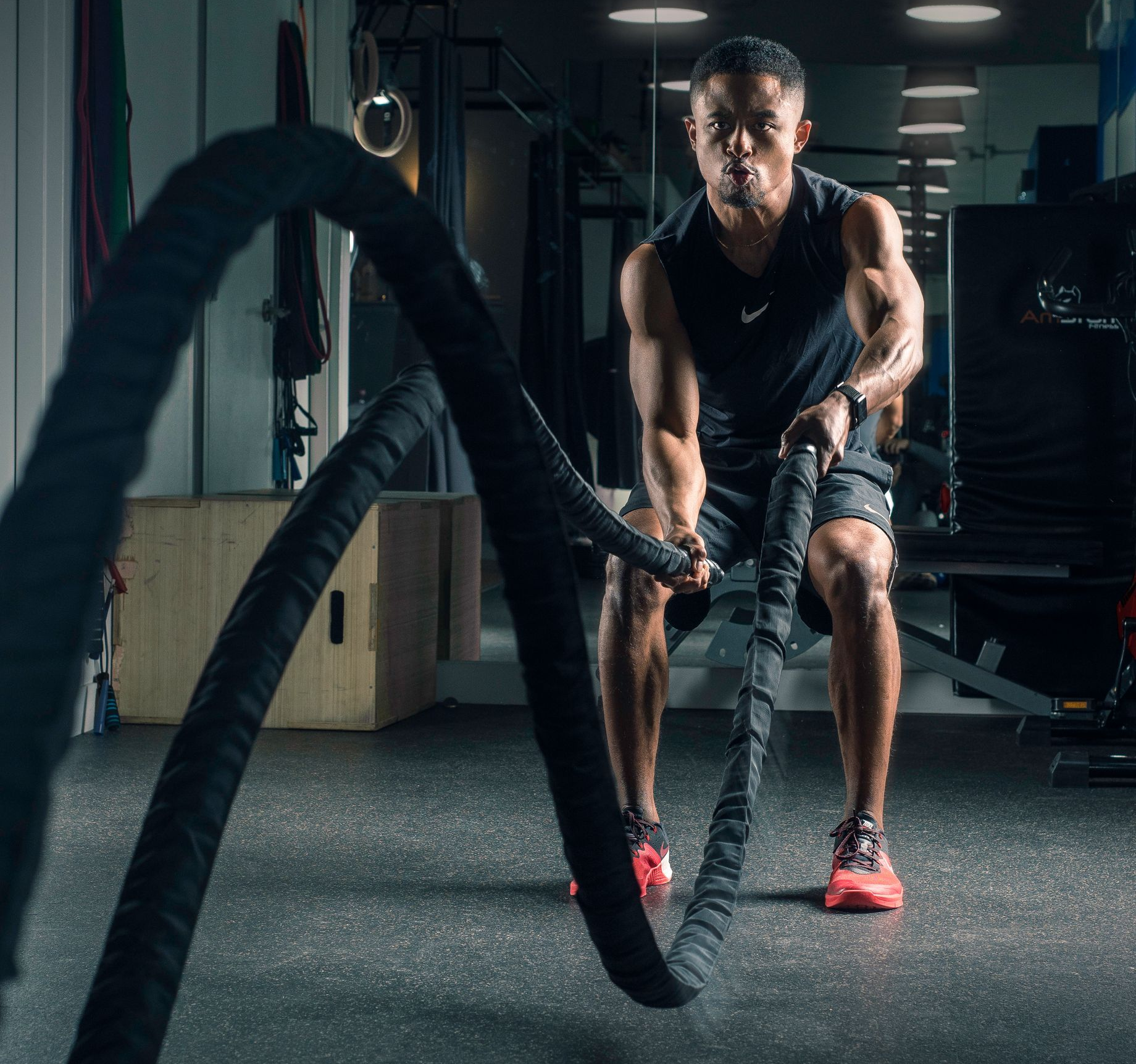 A person in a gym performing a battle rope exercise, creating waves with the ropes while in a focused stance.