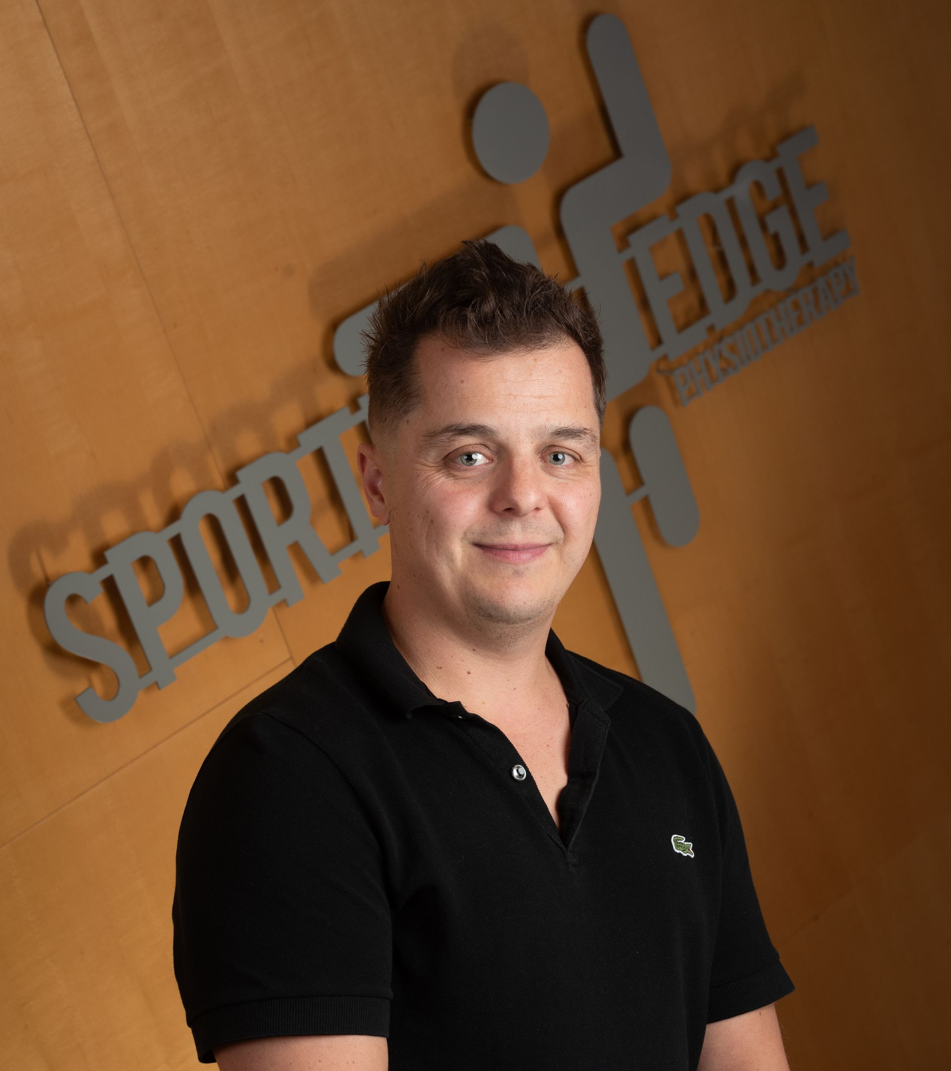 Marco Visconti A person in a black polo shirt smiling in front of a wooden wall with a grey