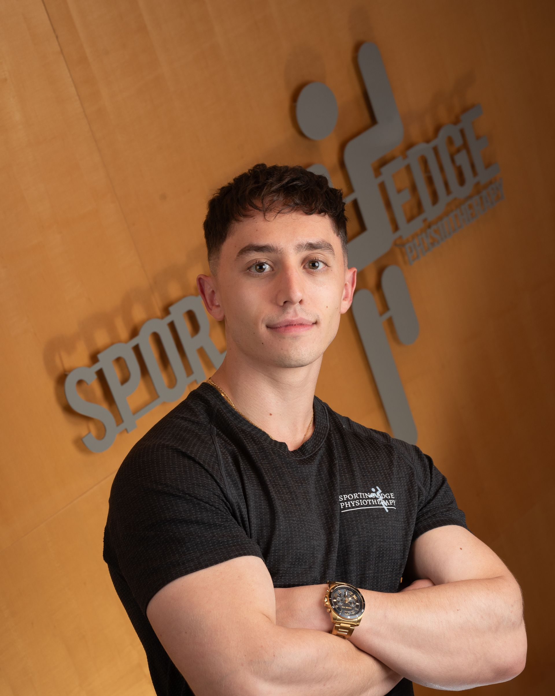 Nicholas Markakos A person with short brown hair wears a black t-shirt and a watch, posing with arms crossed against a Sporting Edge logo background.