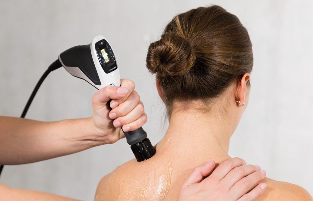 Therapist uses a shockwave device on a woman's shoulder for medical treatment.