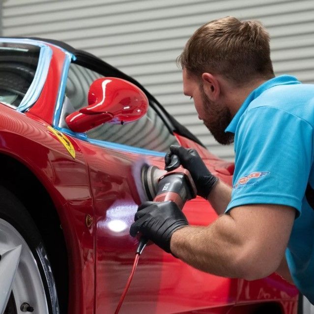 Mechanic polishing a red sports car with a buffer in a garage