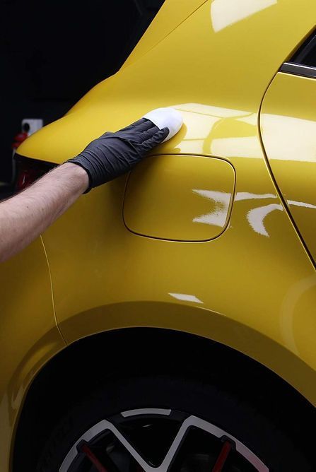 Gloved hand wiping the rear side of a yellow car near the fuel door
