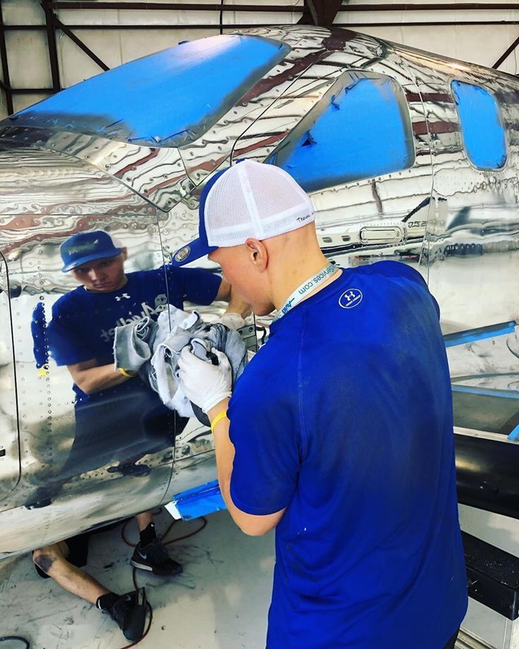 Person polishing a reflective car body in a workshop, with blue panels visible in the paint