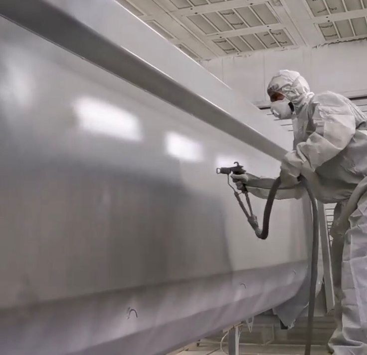 Worker in white protective suit spray-painting a large gray industrial surface in a clean room