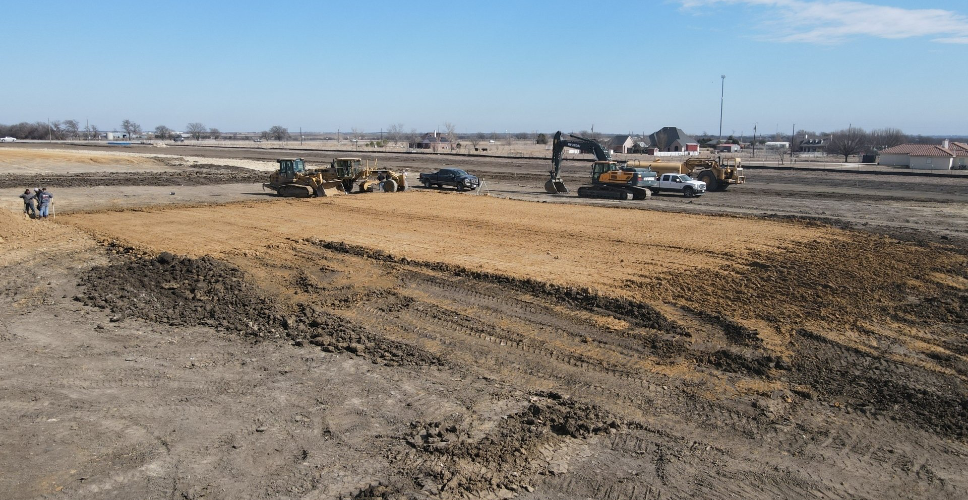 A group of construction vehicles are working on a dirt field