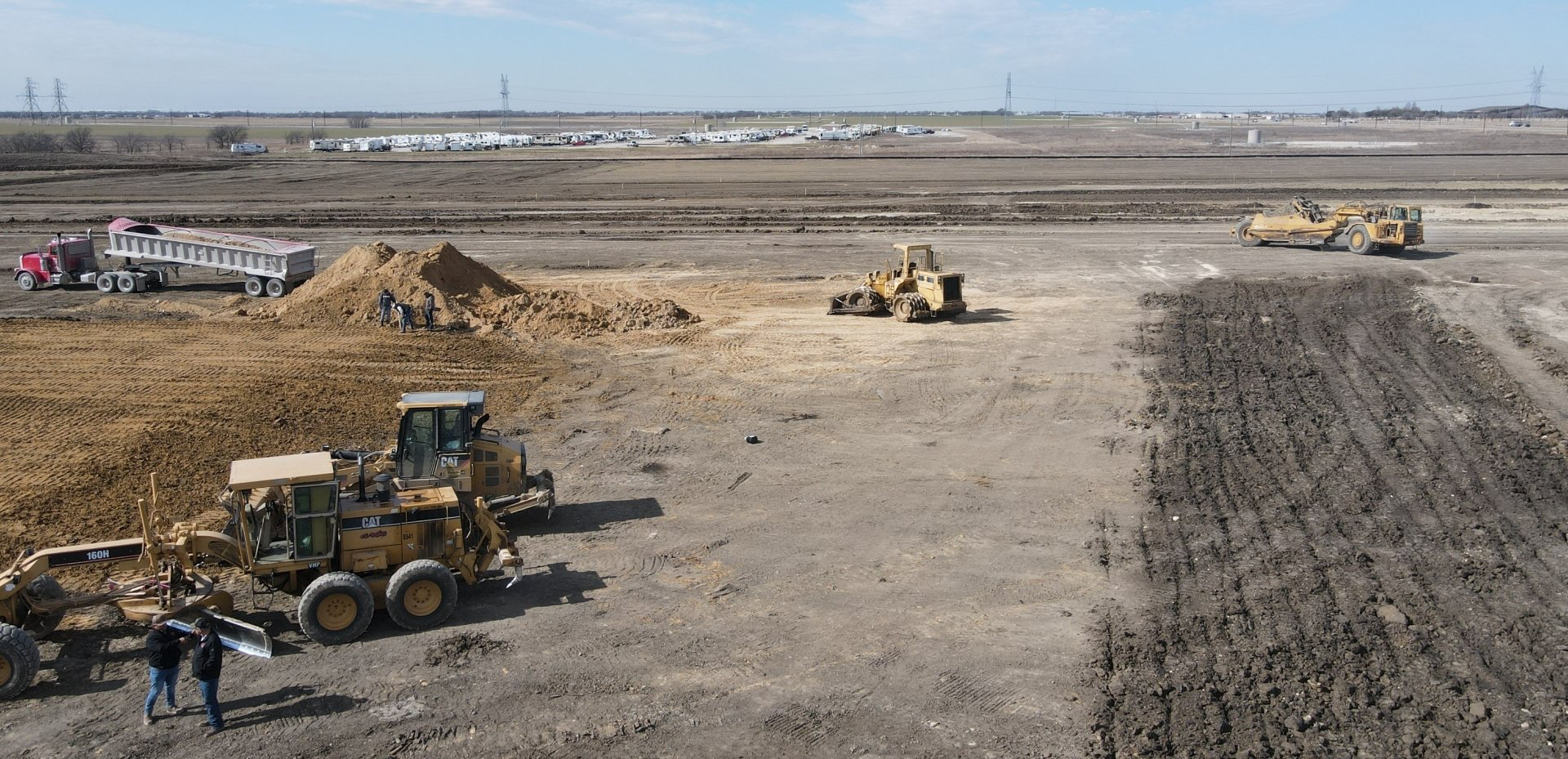 A group of construction vehicles are working on a dirt field.