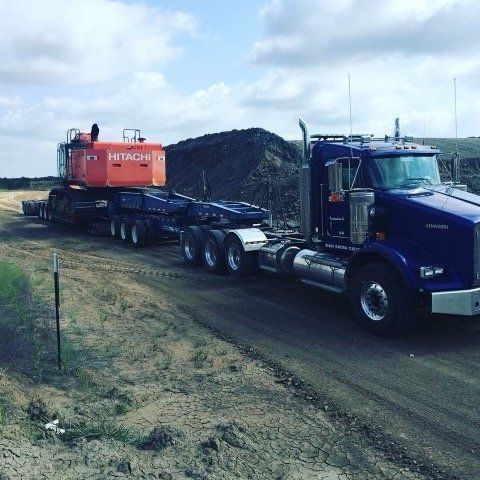 A hitachi truck is driving down a dirt road