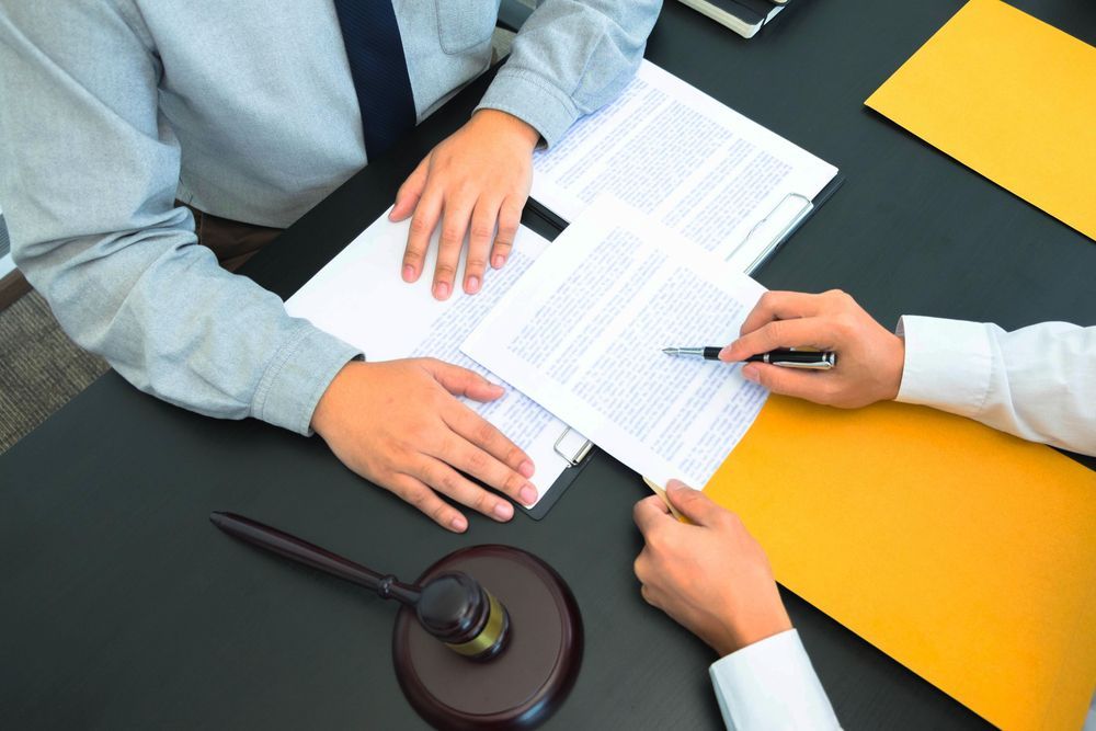 Dos personas revisan documentos en un escritorio con un mazo y una carpeta amarilla.
