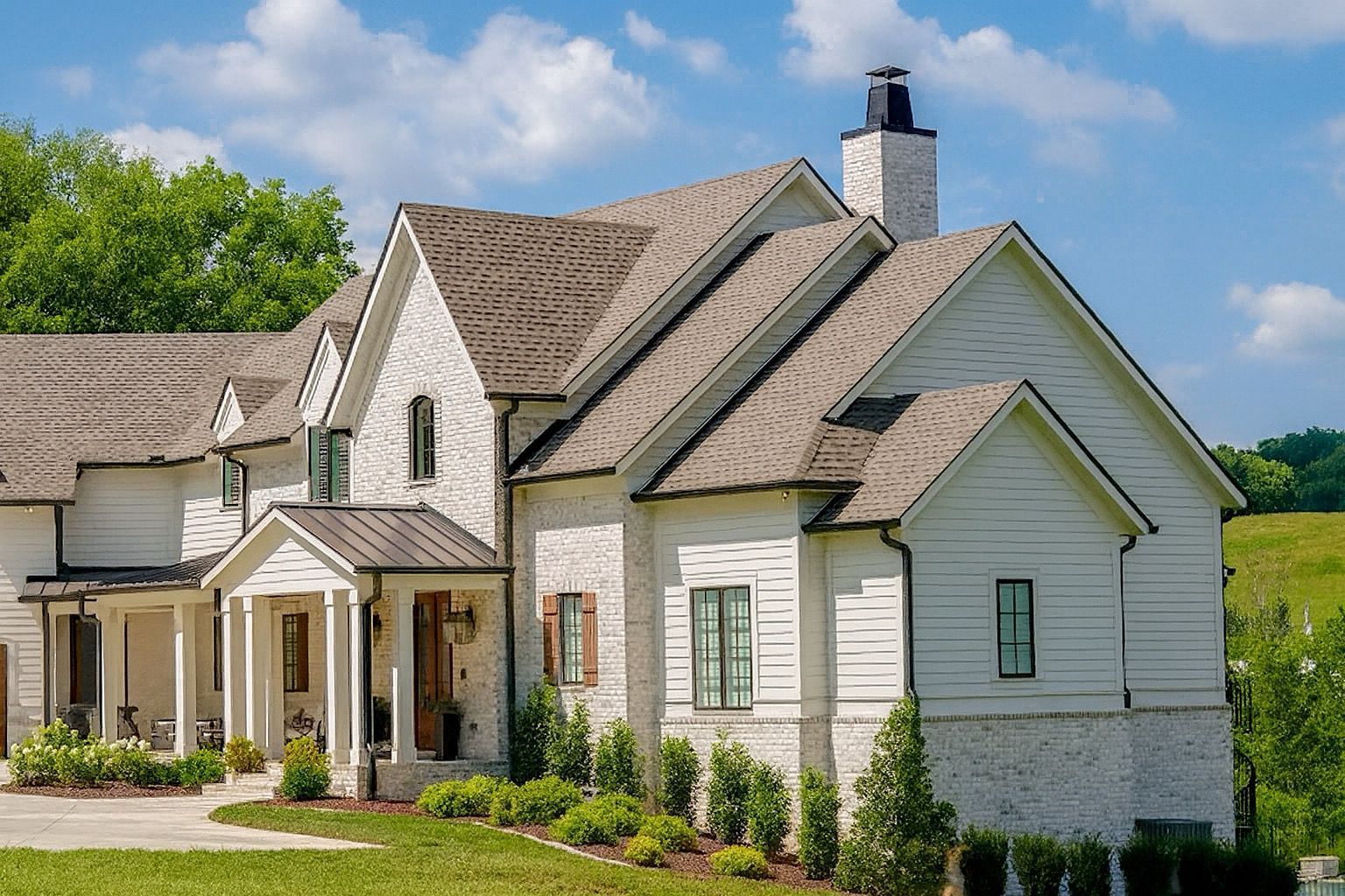 White suburban house with gabled roof, front porch, and green lawn under a sunny sky at redwood roofing