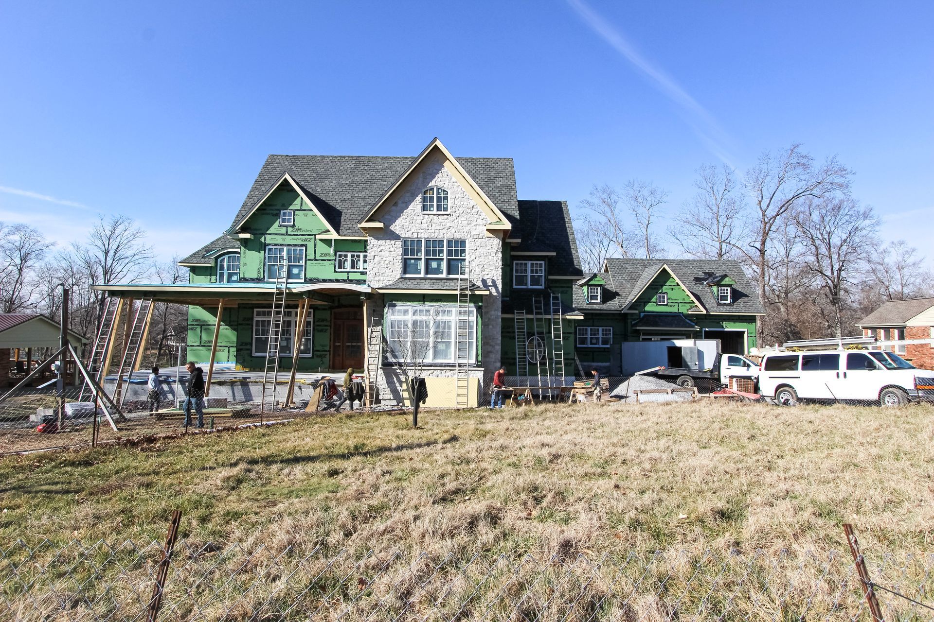 Large Victorian house with green trim, a front porch, and parked vehicles in a grassy yard under a clear sky at redwood roofing and exteriors
