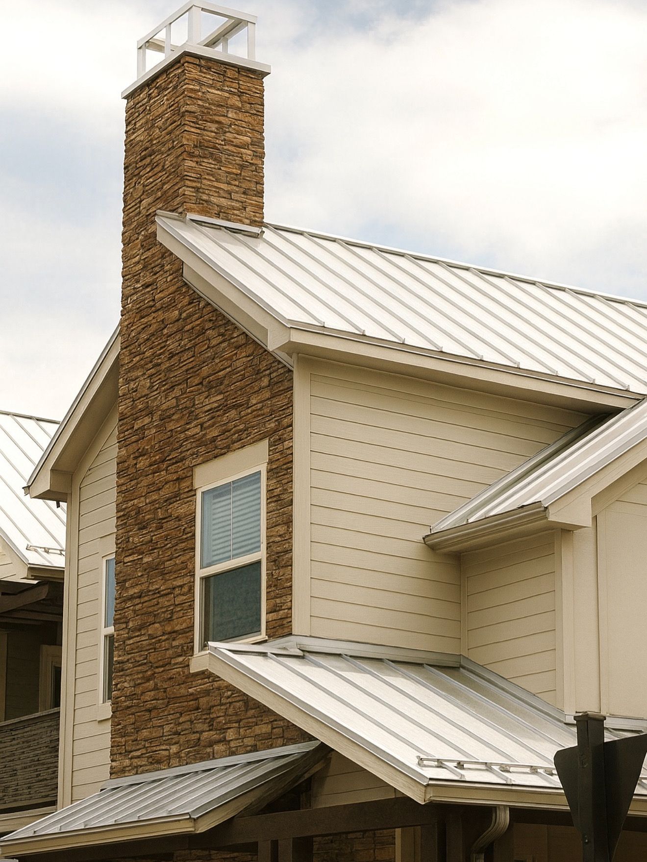 House with tan siding, steep metal roof, and tall stone chimney at redwood roofing and exteriors