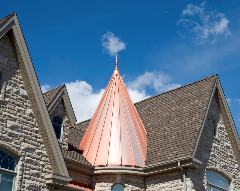 Stone building with steep roofs and a pink copper spire against a blue sky at redwood roofing and exteriors