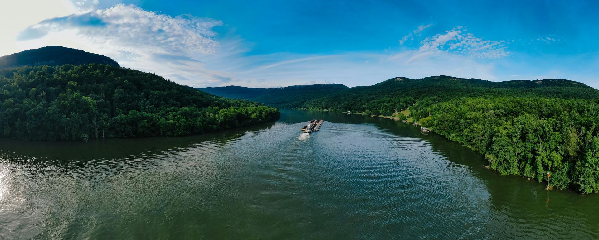 Wide river between green forested hills under a blue sky, with a small boat near the center at redwood roofing in Tennessee 