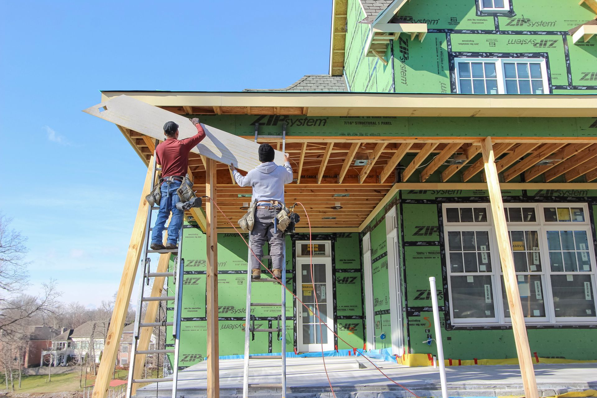 Two workers on ladders installing siding on a green house under construction at redwood roofing