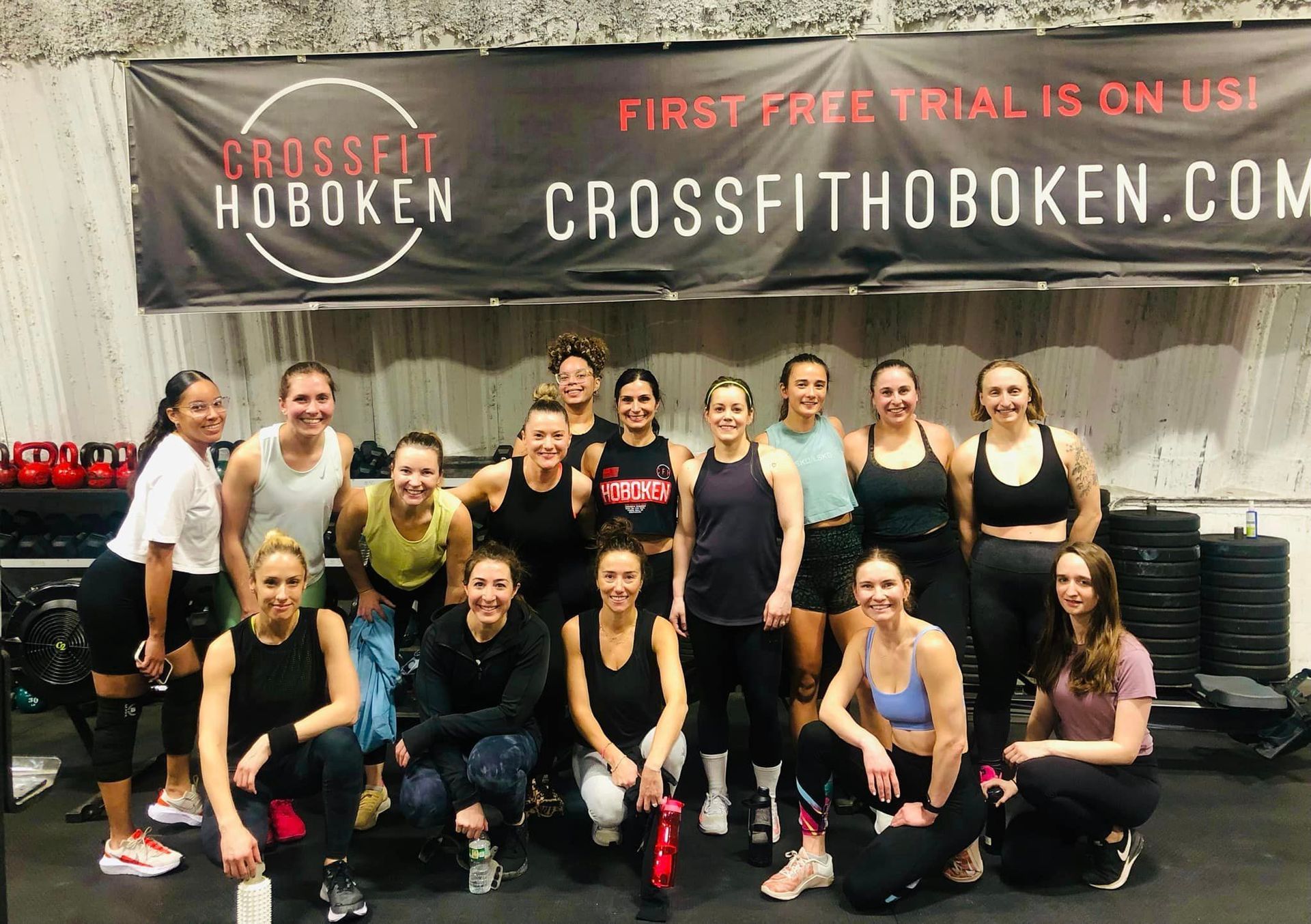 A group of women are posing for a picture in front of a crossfit banner.