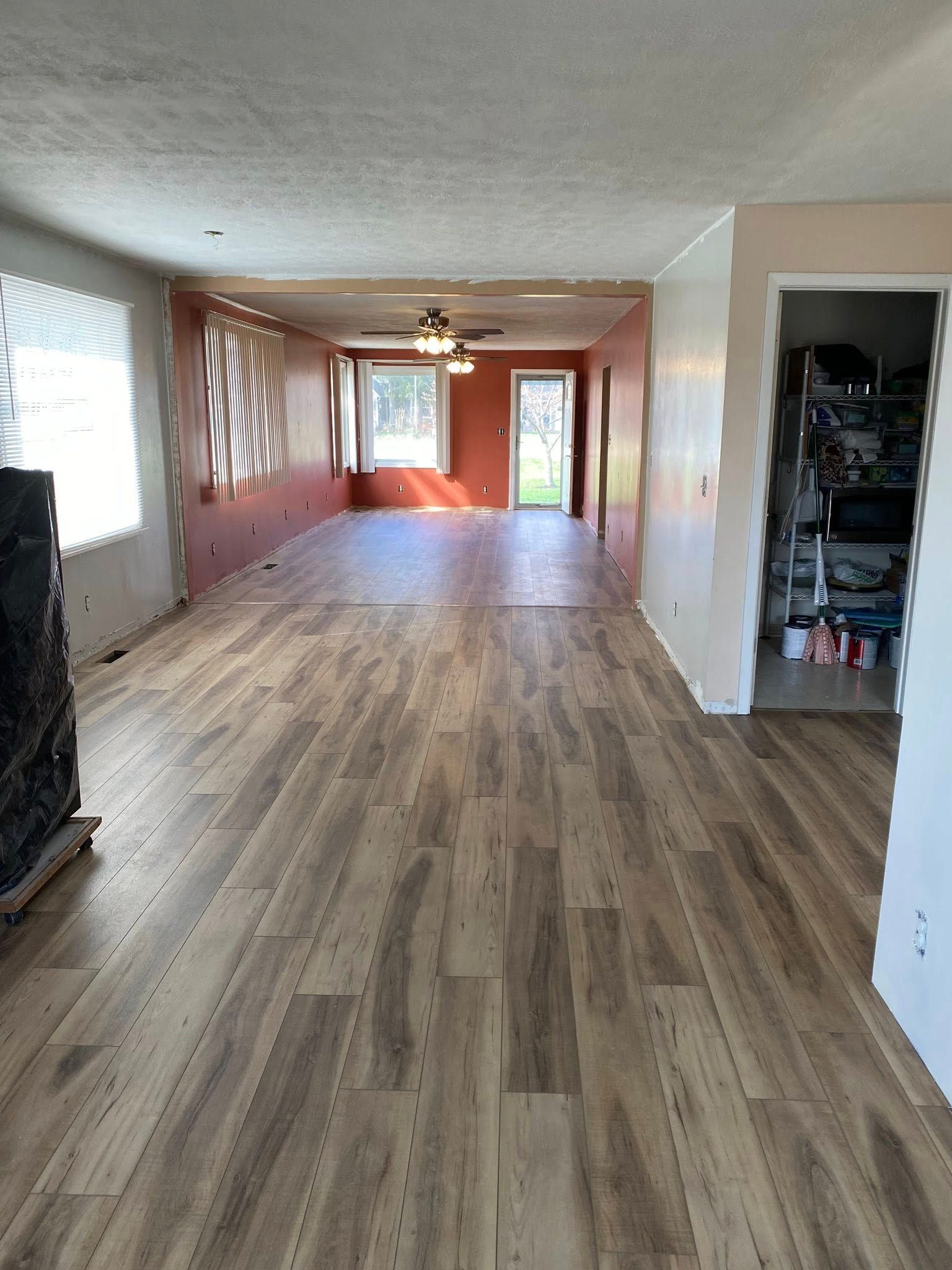 A long, open room with wood-look laminate flooring, light-colored walls, and a separate, darker-painted rear living area.