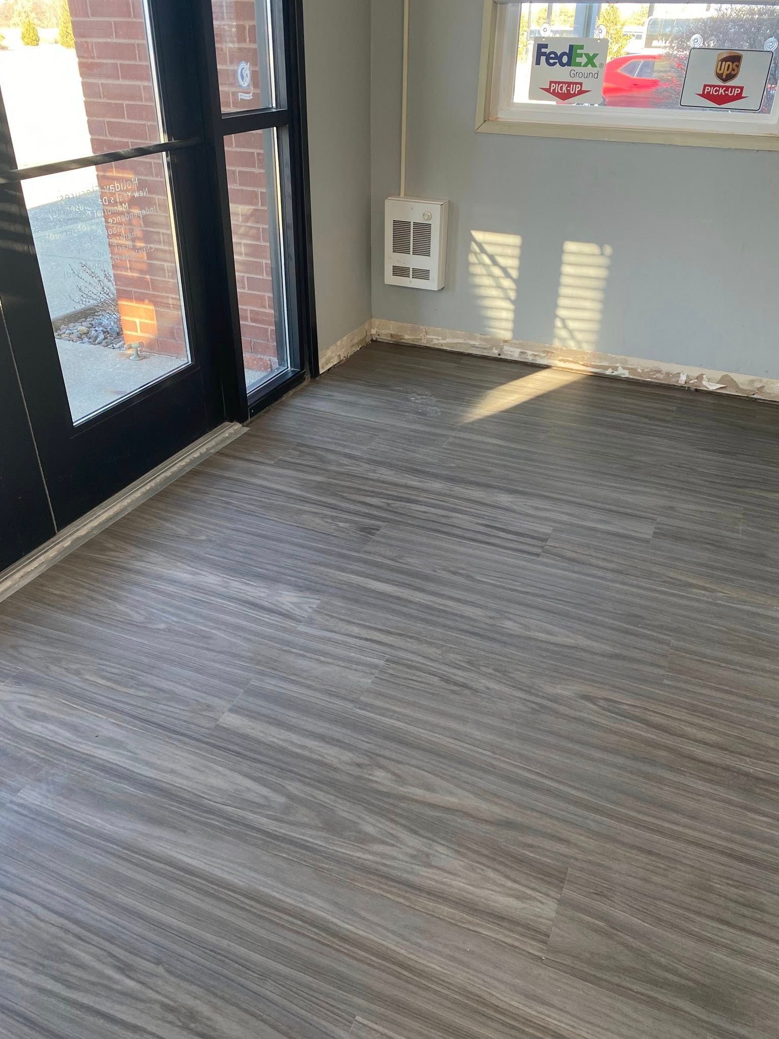 A grey floor with unfinished baseboards in a room with a black-framed glass door and a FedEx sign on the window.