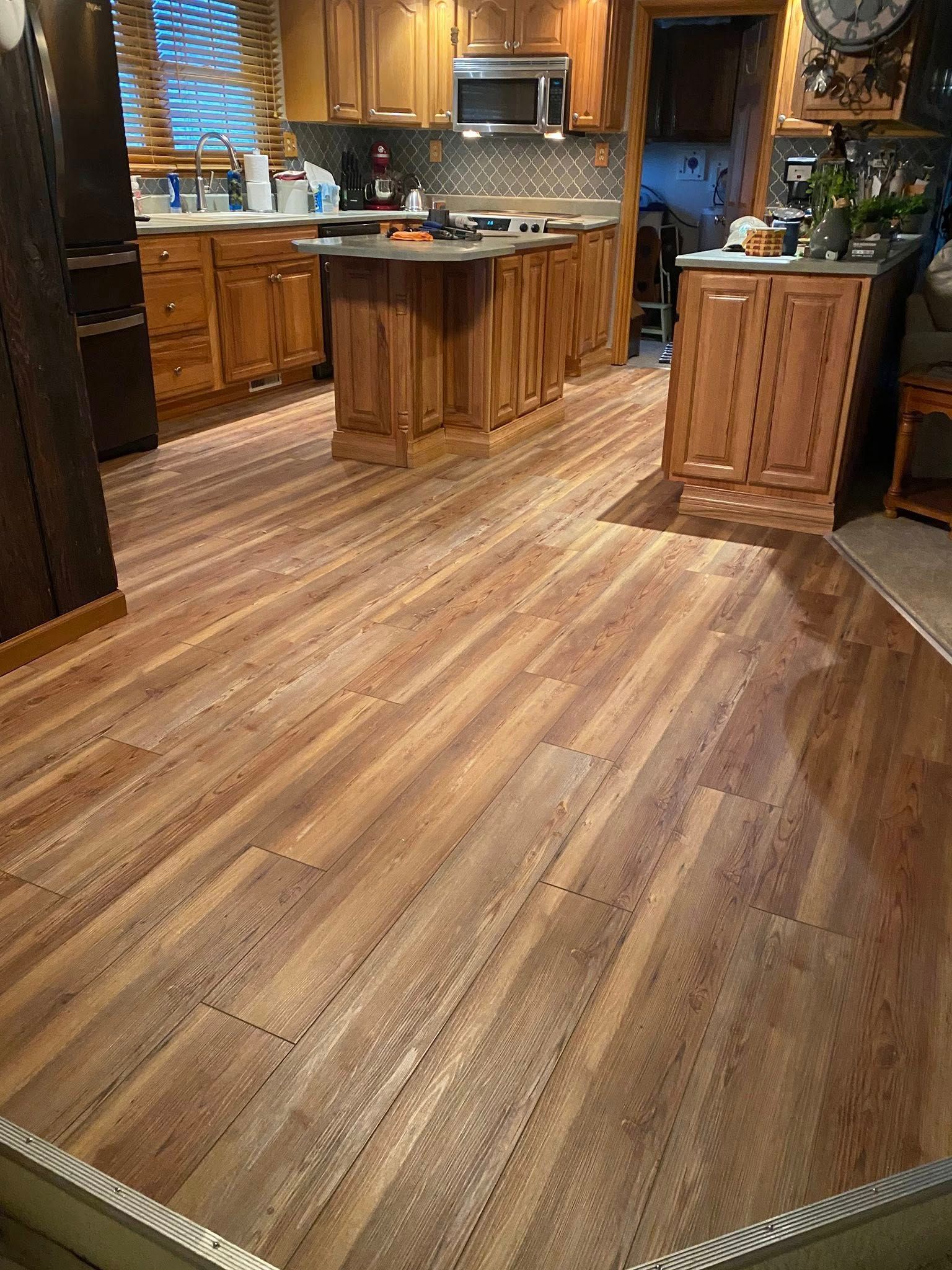 A wood-floored kitchen with oak cabinetry and a central island, viewed from an adjacent room.