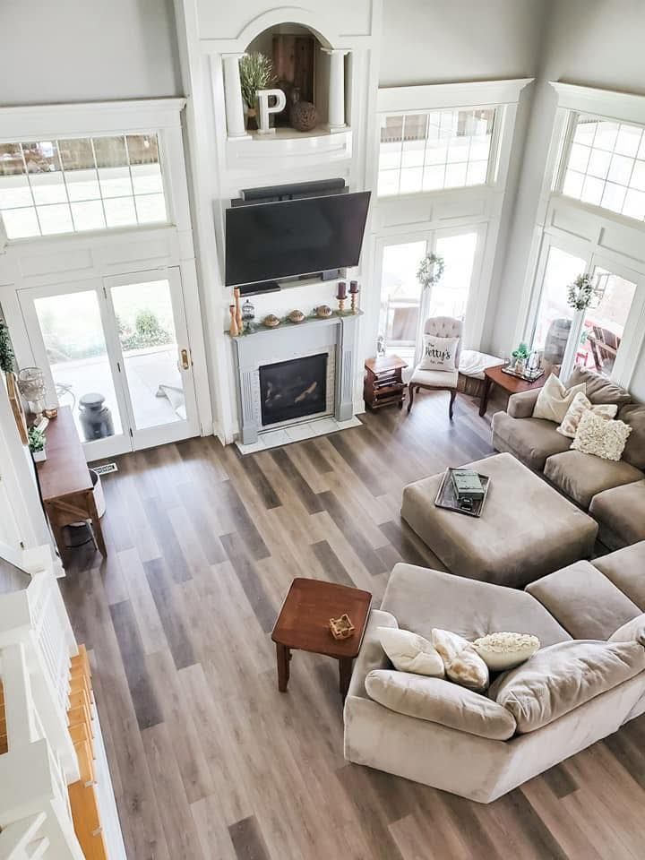 A high-angle view of a living room featuring wood-look floors, a sectional sofa, ottoman, and a fireplace with a TV.