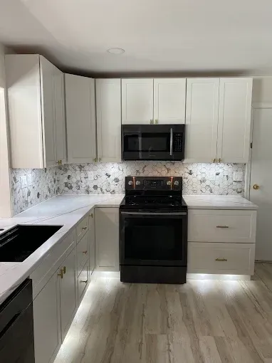 A kitchen with white cabinets, light wood floors, a floral backsplash, and black appliances.
