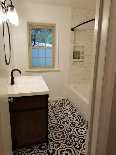 A modern bathroom features a dark wood vanity, white countertop, black fixtures, and patterned black and white floor tiles.