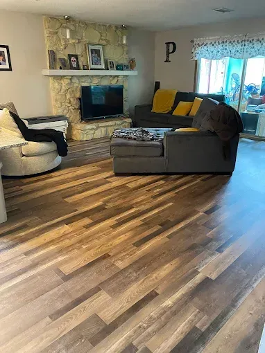 A living room featuring multi-toned hardwood floors, a stone fireplace with a television, and a gray sofa and armchair.