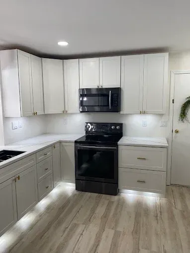 A renovated kitchen featuring white cabinets, stainless steel appliances, marble countertops, and light wood flooring.