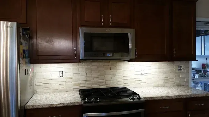 A kitchen with dark wood cabinets, stainless steel appliances, speckled countertops, and a textured white stone backsplash.