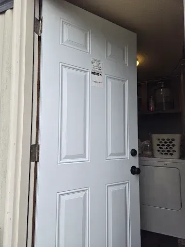 A white, six-panel door standing slightly open to a laundry area with a white washing machine and a laundry basket.