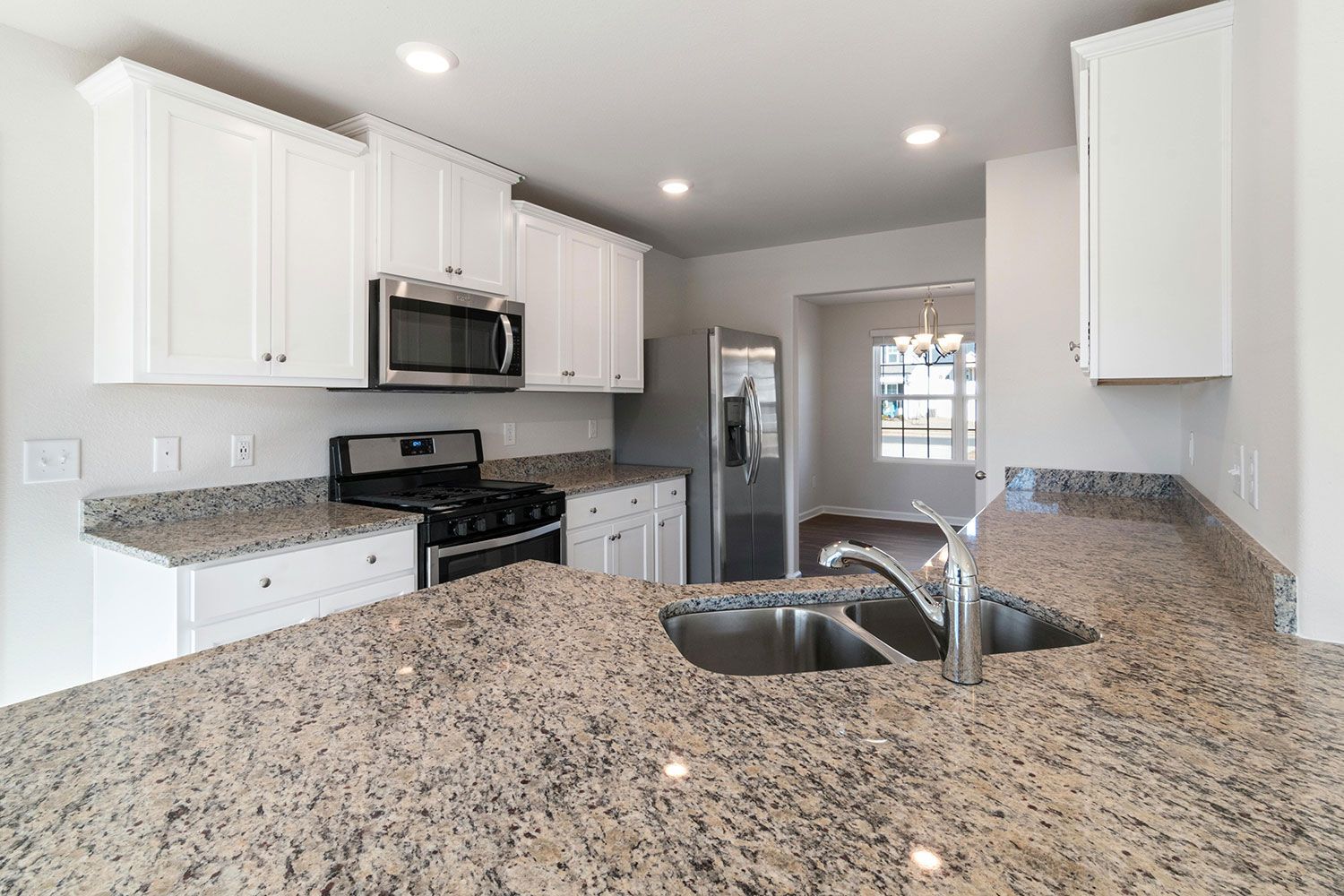 A kitchen with white cabinets, granite countertops, stainless steel appliances, and a double-basin sink.