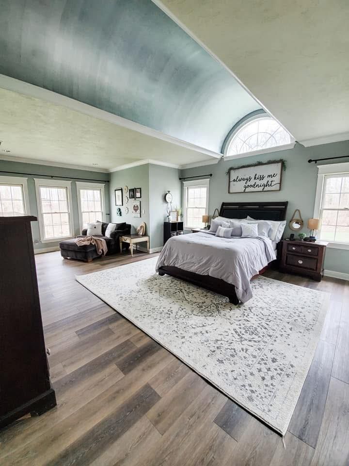 Spacious bedroom with a barrel-vaulted ceiling, a bed, a rug, dark wood floors, and a lounge area by the windows.