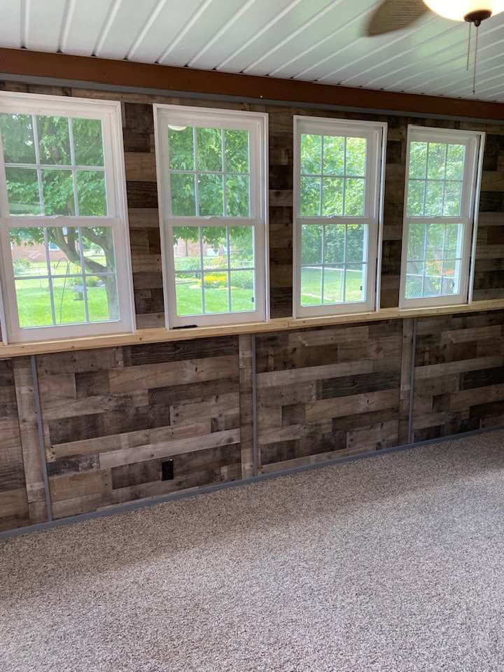 Sunroom wall with rustic horizontal wood paneling and four white-framed windows above a wooden ledge.