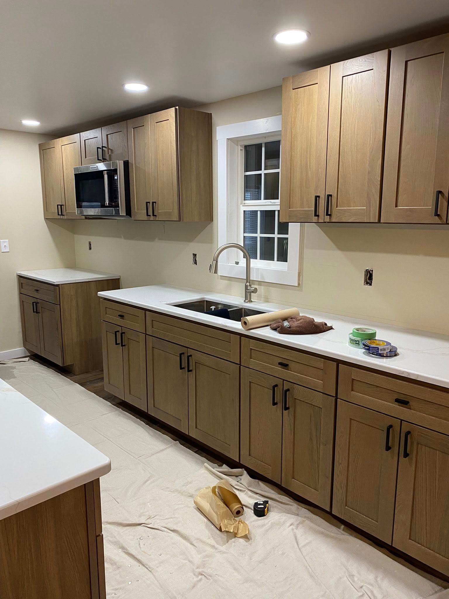 A kitchen featuring light-wood cabinets, white countertops, a stainless steel microwave, and a window above the sink.