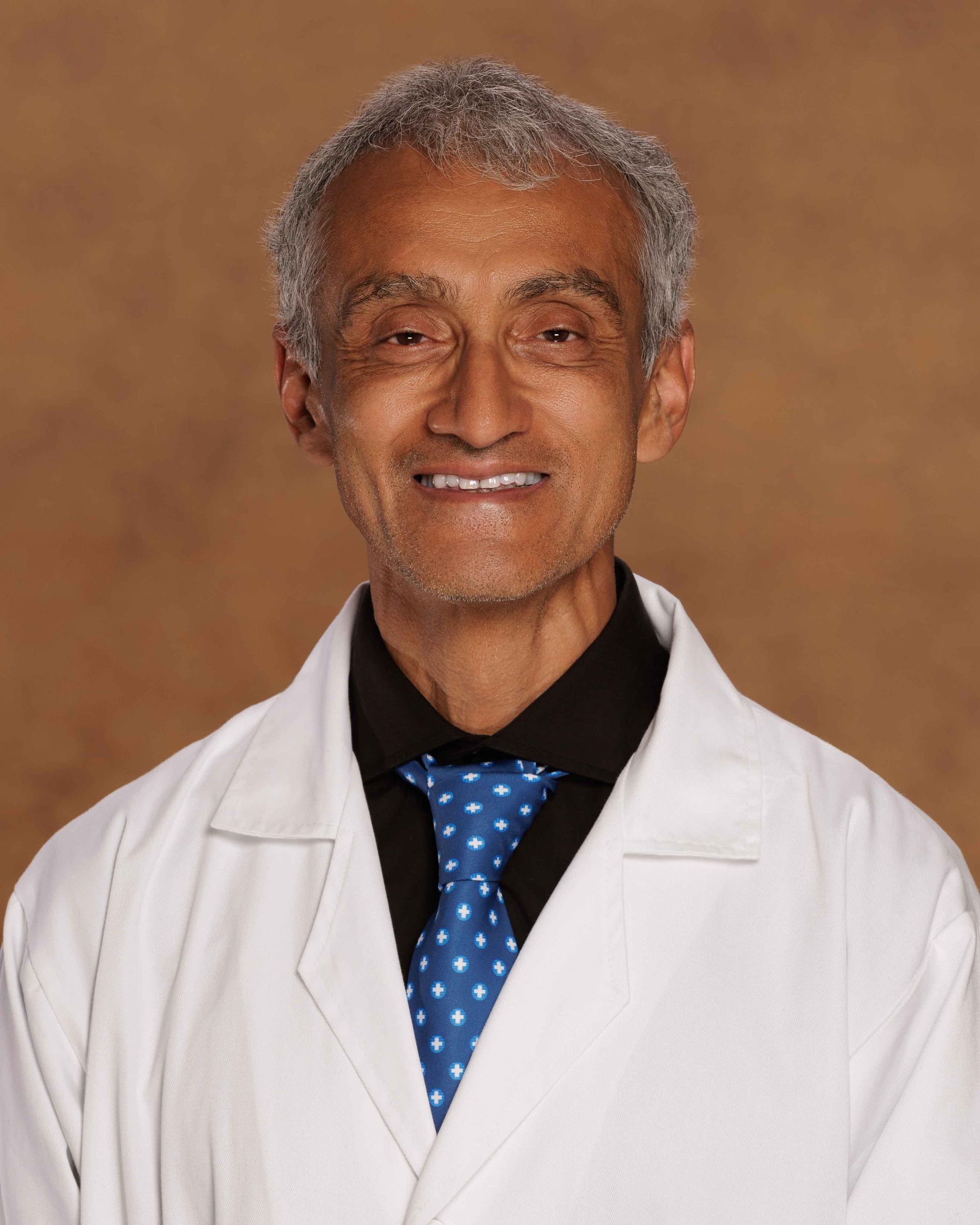 A man in a white coat and blue tie smiles for the camera