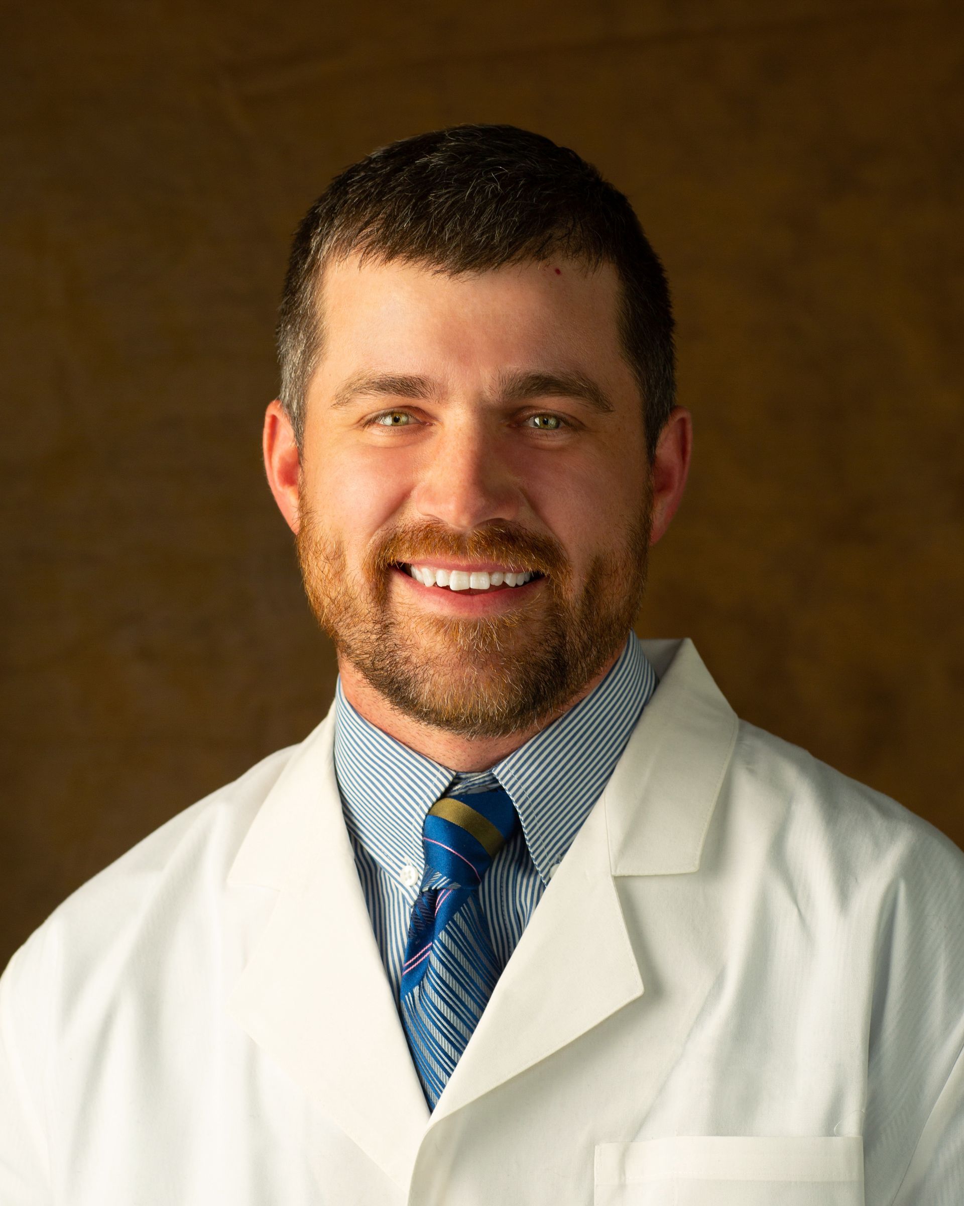 A man in a lab coat and tie is smiling for the camera.