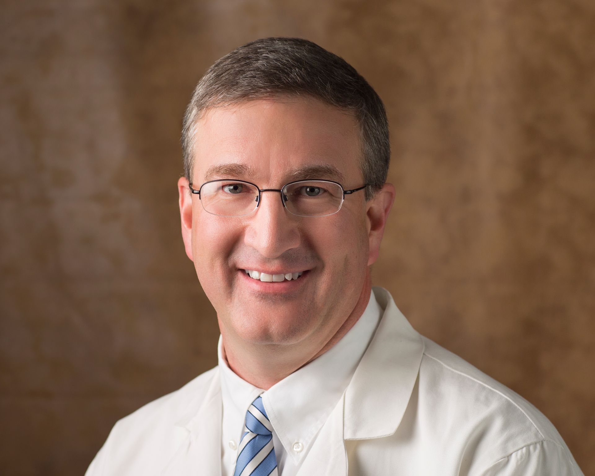 A man wearing glasses and a white coat is smiling for the camera