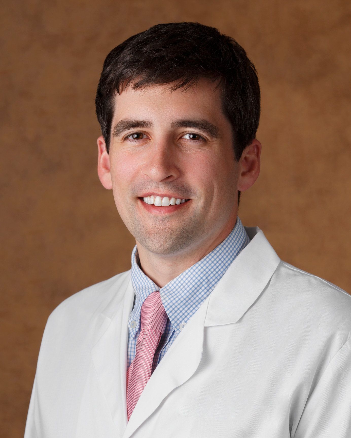 A man in a white coat and pink tie smiles for the camera