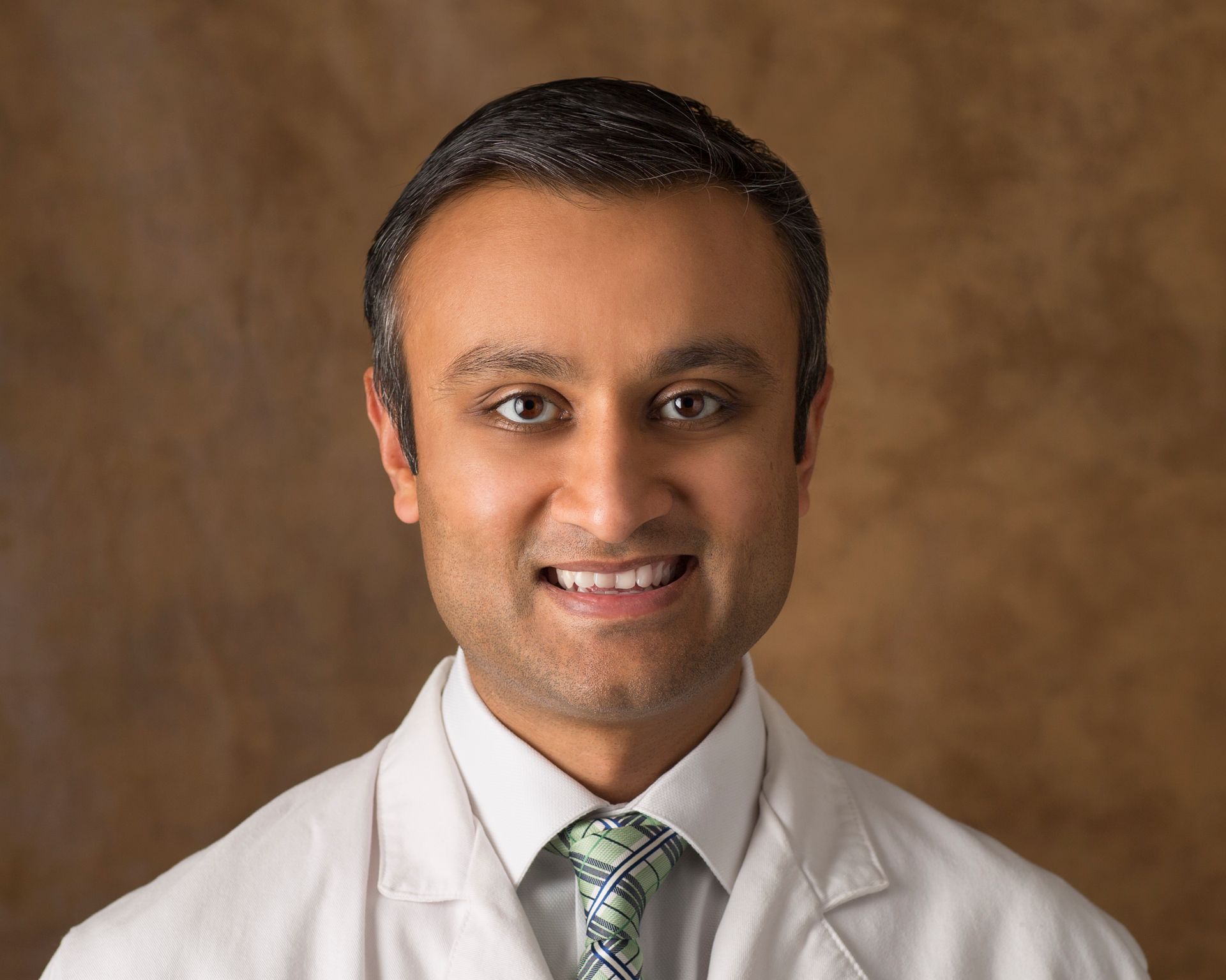 A man in a white coat and tie is smiling for the camera