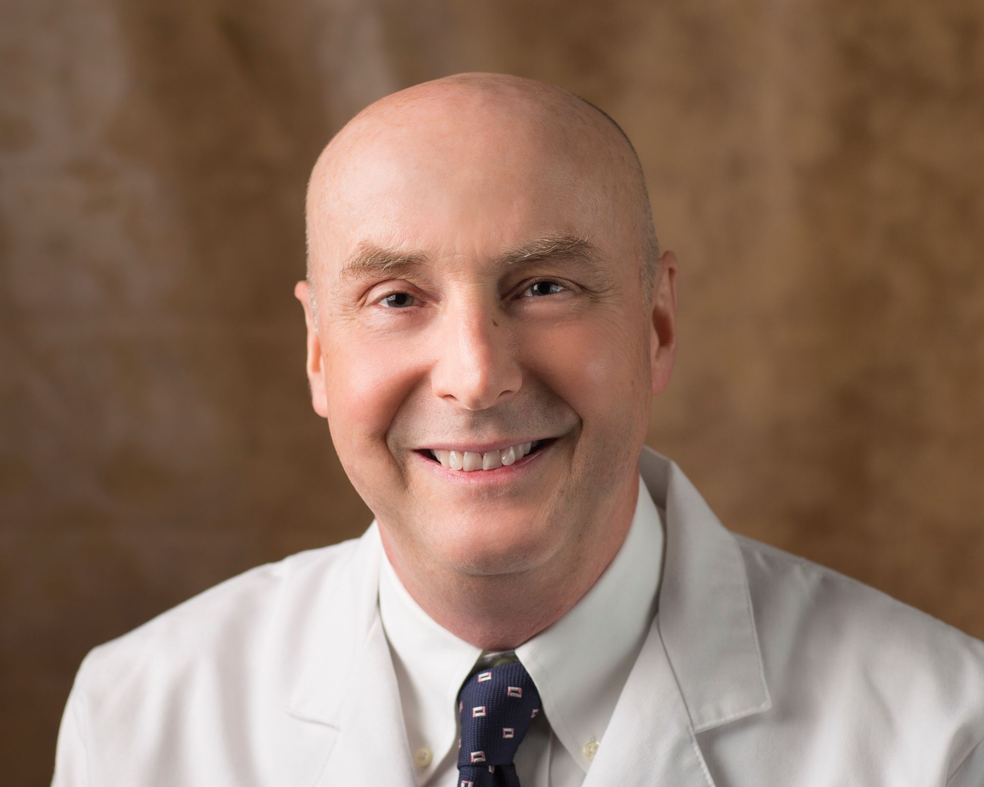 A bald man wearing a white coat and tie is smiling for the camera.