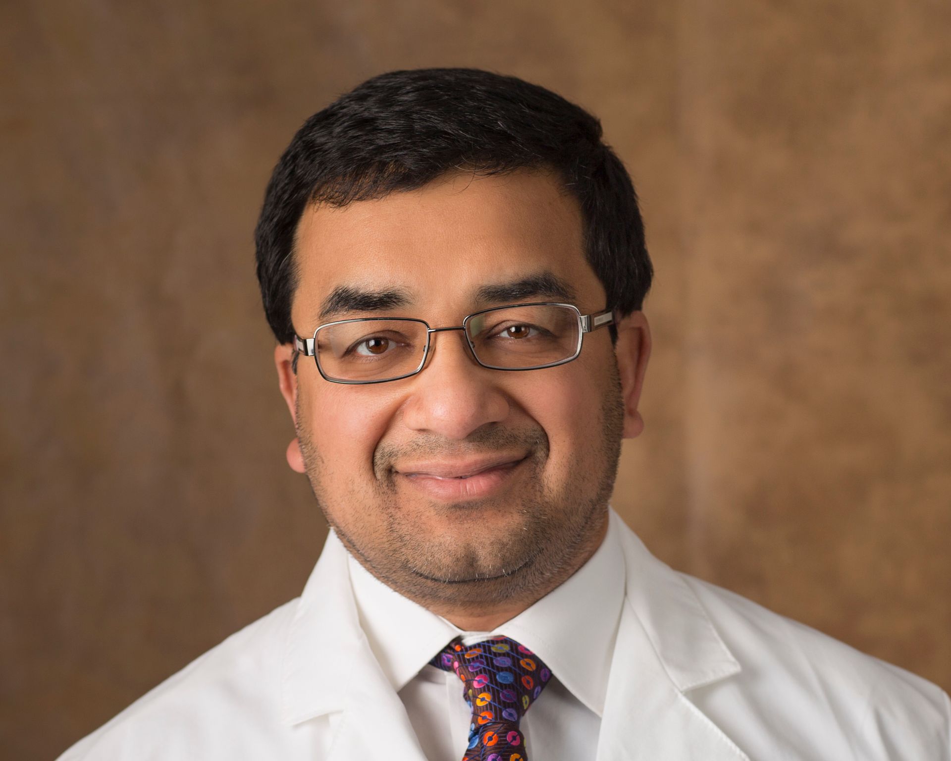 A man in a white coat and tie is smiling for the camera.