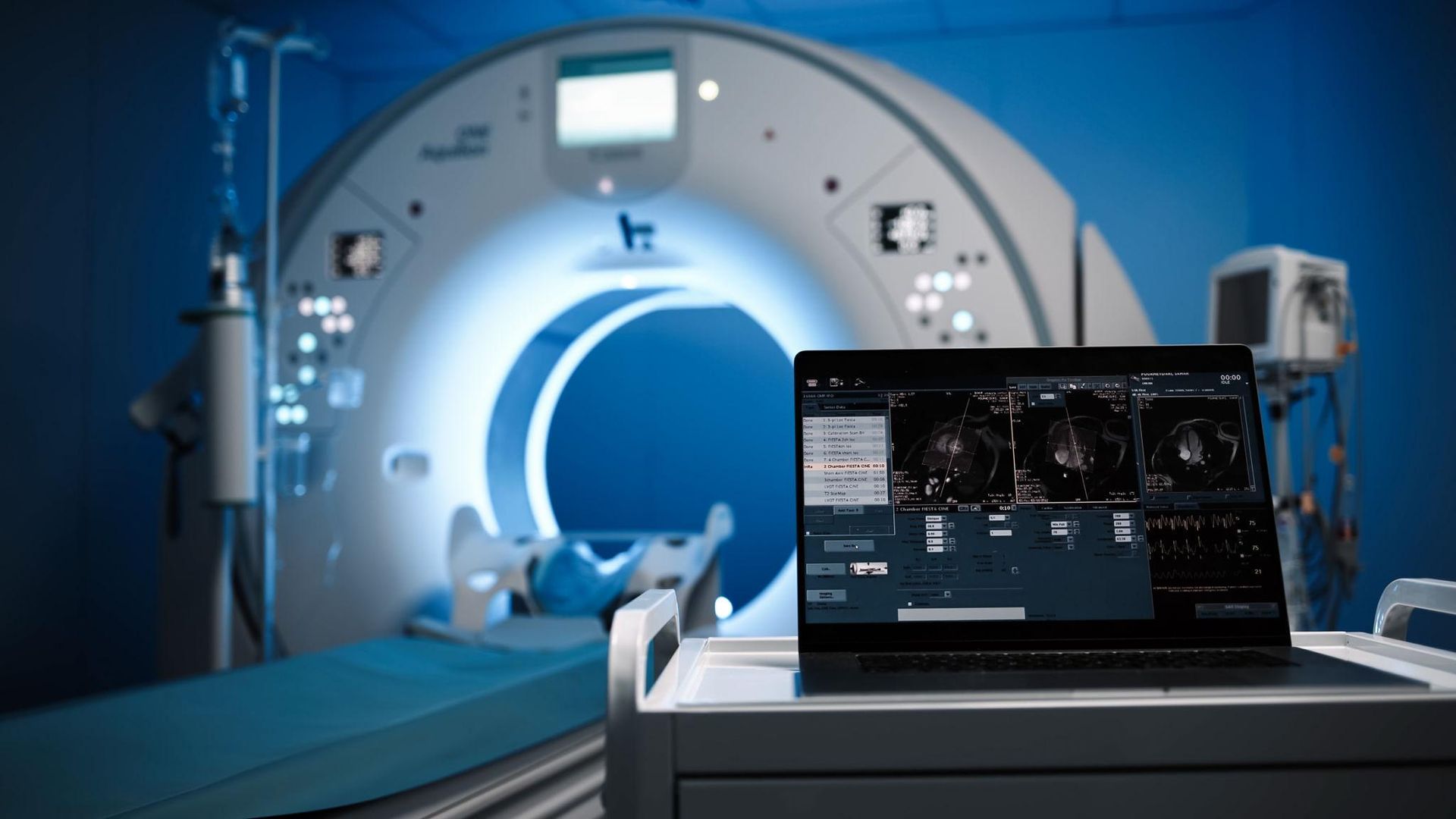 Hospital MRI scanner with a patient table and a laptop displaying medical scans in the foreground