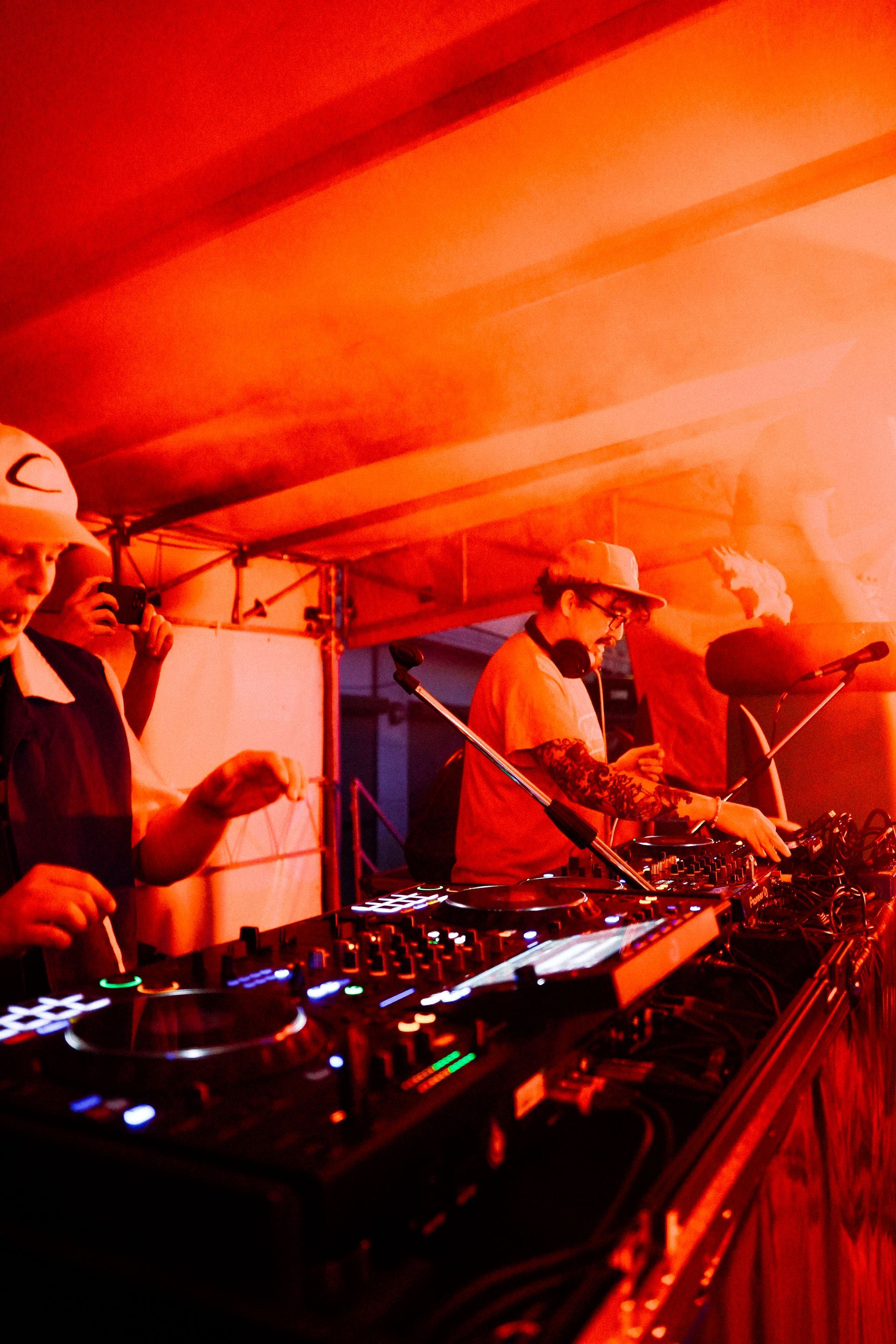 Deux DJ mixent de la musique sur scène sous une lumière rouge.