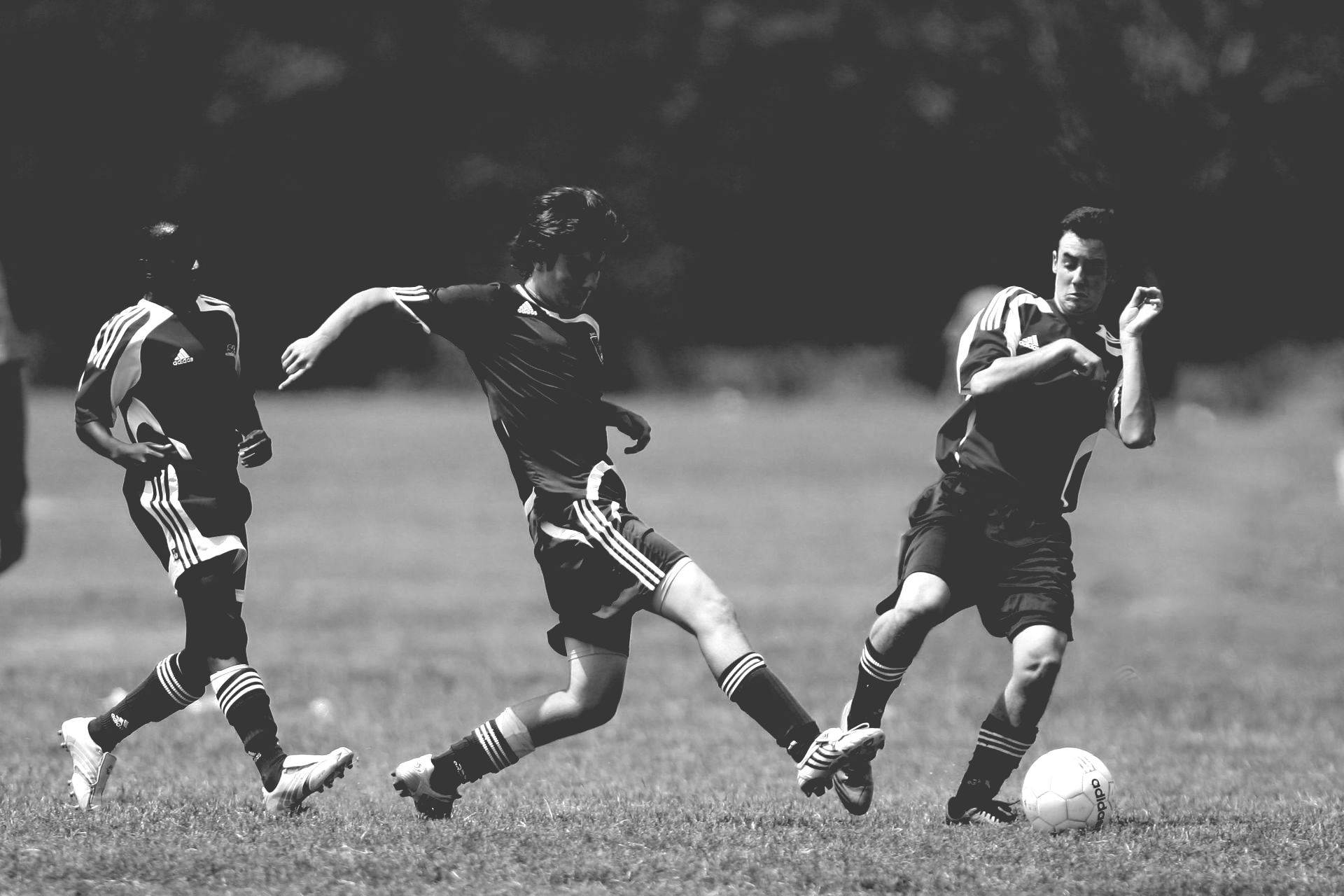 Des joueurs de football sur un terrain herbeux ; l'un d'eux frappe le ballon, deux autres se trouvent à proximité.